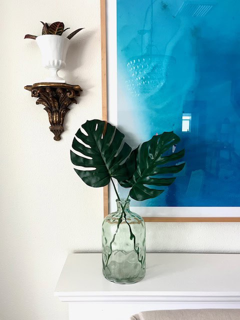 Faux monstera leaves in vase on white mantle