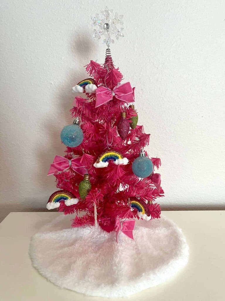 Pink Christmas tree decorated with rainbows, bows, and colorful ornaments for festive holiday interior design.