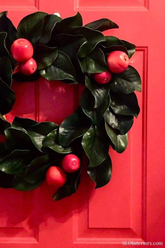 Festive holiday wreath with green leaves and red berries on a red door.