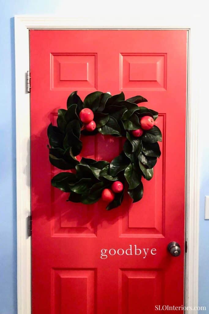 A colorful holiday wreath with red berries hanging on a red door.