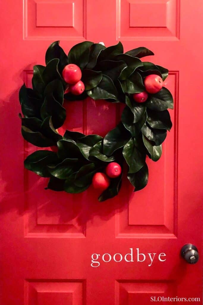A lush holiday wreath with red berries hanging on a vibrant red door.