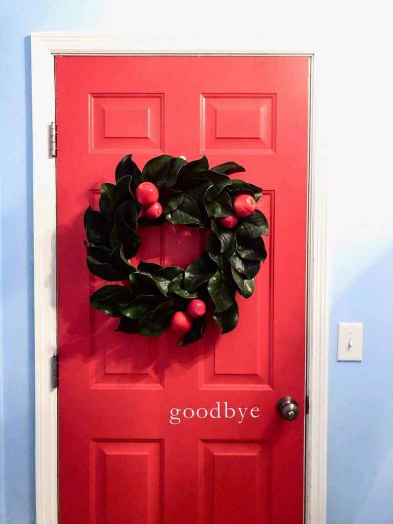 A festive holiday wreath on a red door with "goodbye" written below.
