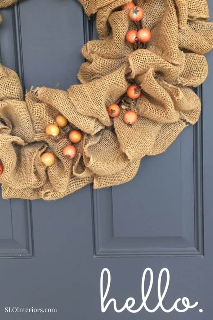 A festive burlap wreath with orange berries hanging on a dark blue door.