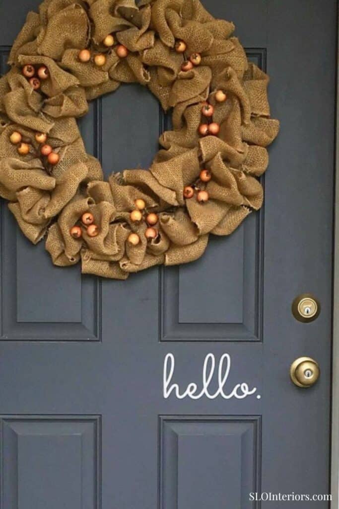 Festive burlap wreath with orange berries on a dark door with "hello" sign.
