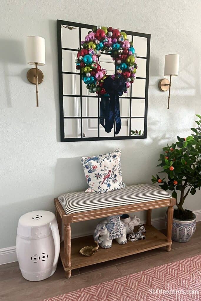 Festive holiday wreath with colorful ornaments hanging on wall decor in entryway.