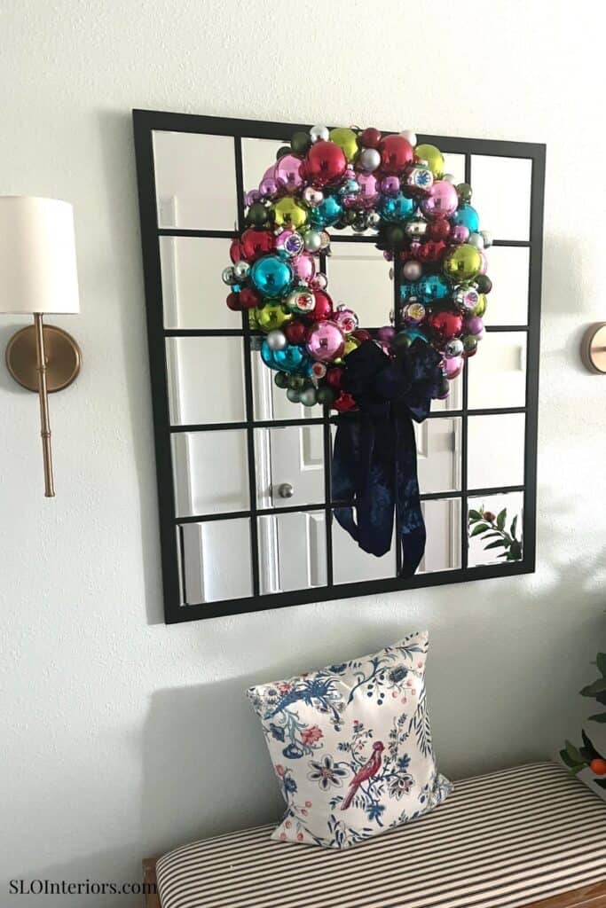 Festive Christmas wreath with colorful ornaments hanging on a black grid mirror in a cozy living roo.