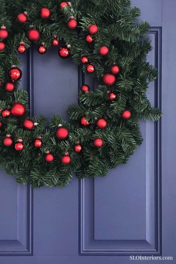 Festive Christmas wreath with red ornaments on a blue door, holiday decor, SLO Interiors.