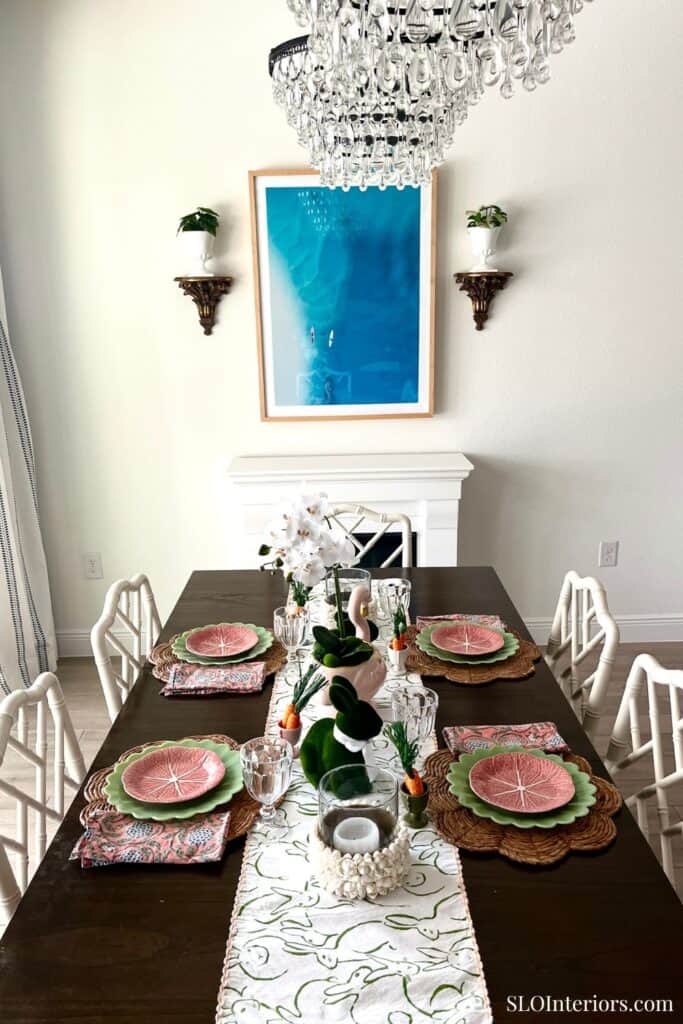 Elegant dining room with chandelier, floral centerpiece, and pink and green tableware.