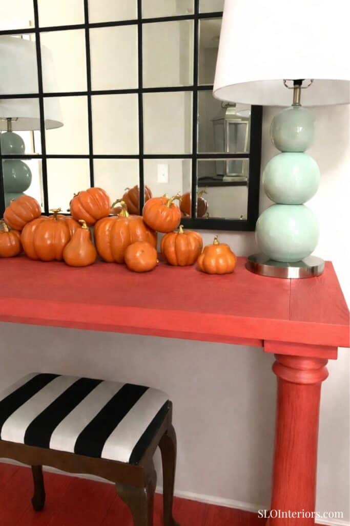 Pumpkin decor on red table with modern lamp and black-and-white striped chair in interior space.