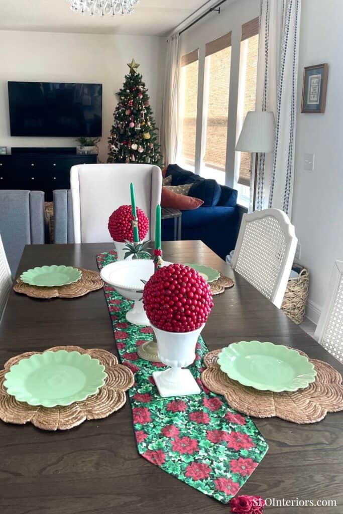 Festive holiday dining table with Christmas decorations and a decorated tree in the background.