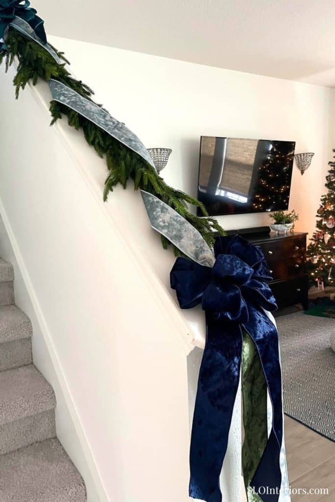 Festive staircase decorated with greenery, silver ribbon, and a large blue bow for Christmas celebra.