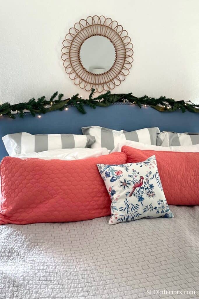 Cozy bedroom with decorative pillows, mirror, and holiday garland decor.