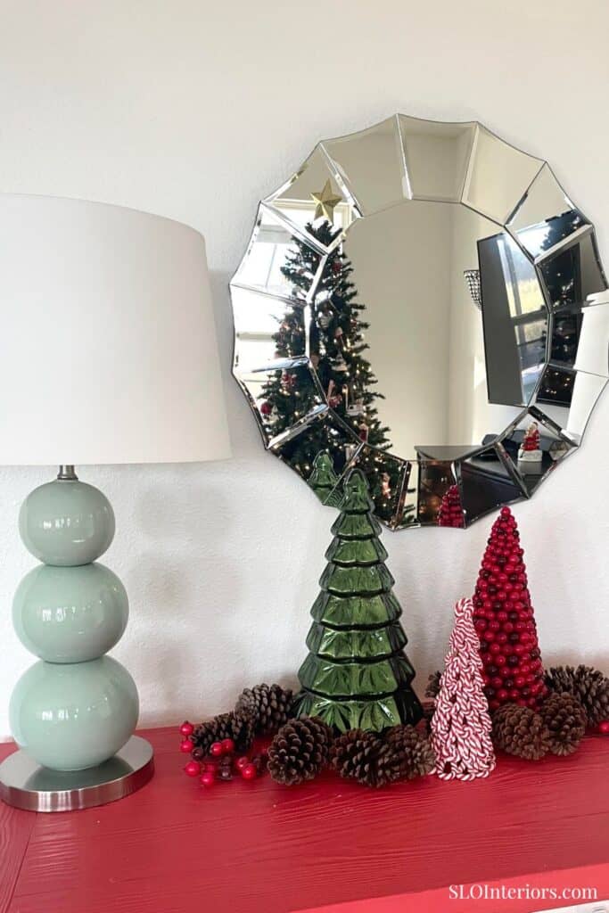 Festive Christmas decorations with a mirror, tree, and ornaments on a red table.