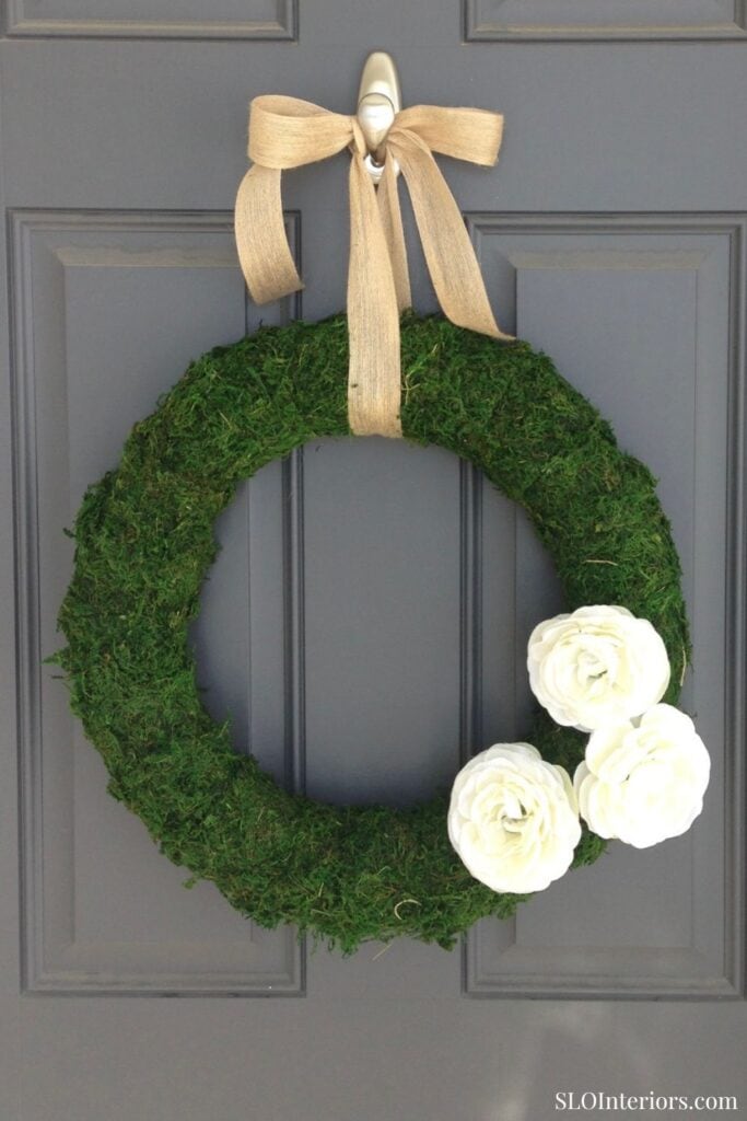 DIY Moss wreath hanging on gray front door with burlap ribbon and three white flowers
