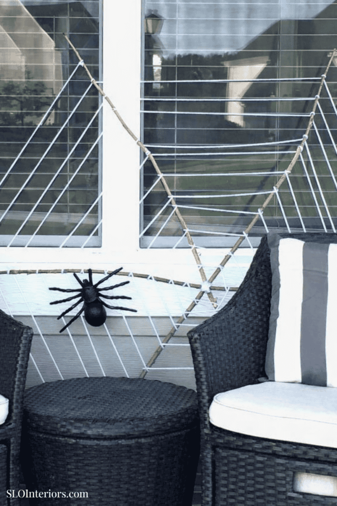 Spooky Halloween spider decoration on porch with outdoor furniture and window backdrop.