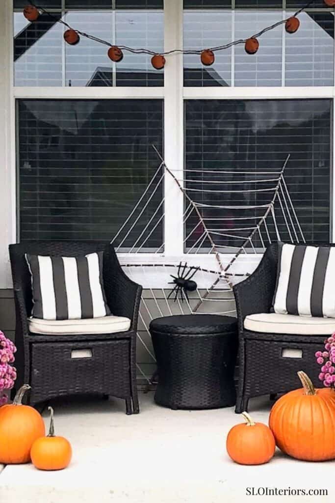 Spooky Halloween porch decor with pumpkins, spider, and string lights.
