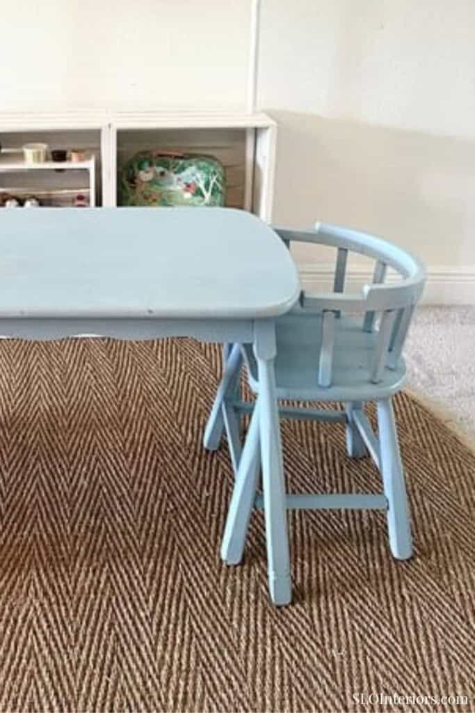 A light blue children's table and chair set in a cozy room with a textured rug.