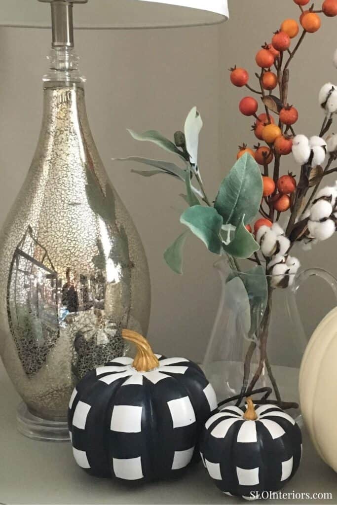 A decorative black and white checkered pumpkin with a gold stem, surrounded by autumnal branches and.