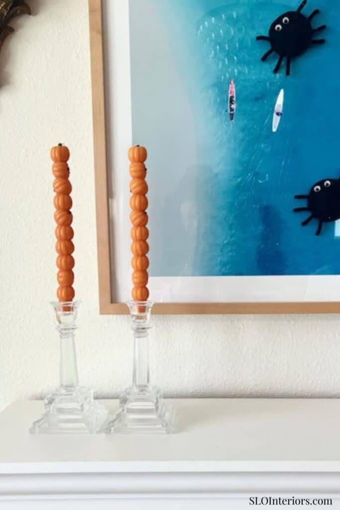 Orange beaded candles on glass holders in modern interior decor with ocean-themed artwork.