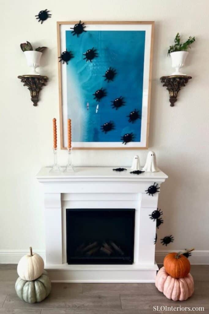A colorful framed artwork with black bug decorations on a white fireplace mantel and wall shelves.