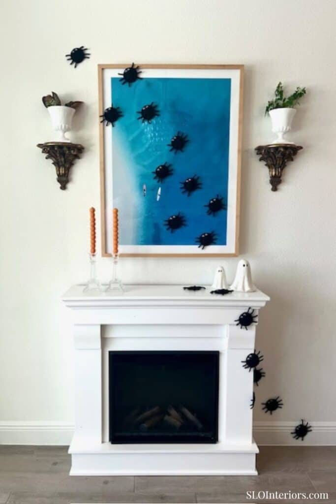 Modern white fireplace with black decorative bugs and framed blue artwork.