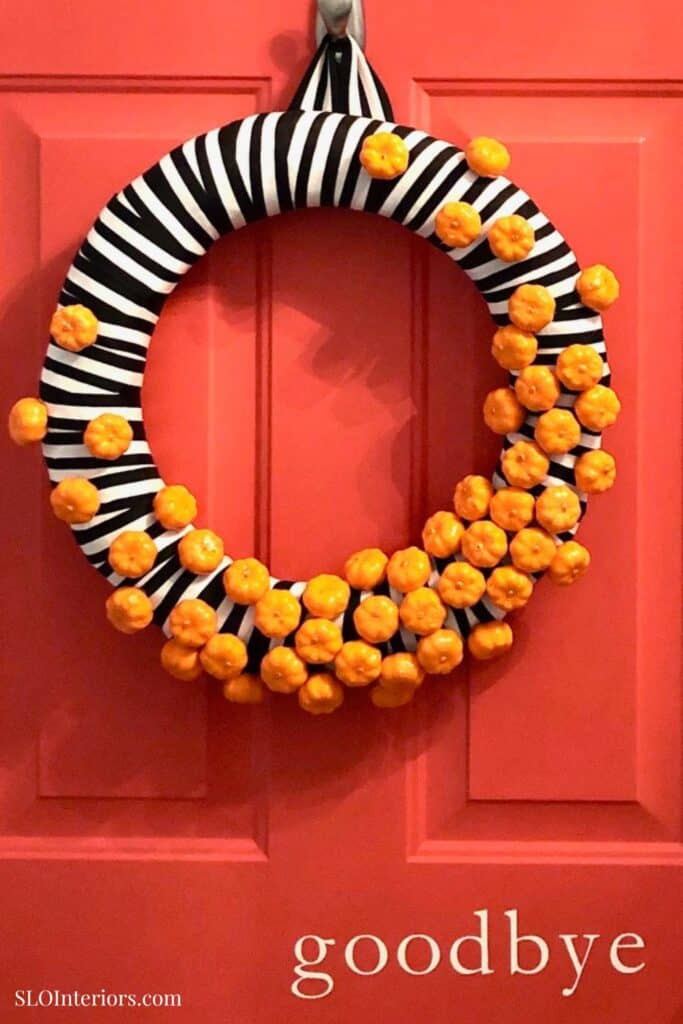 Black and white striped wreath with orange pom-poms hanging on a pink door.