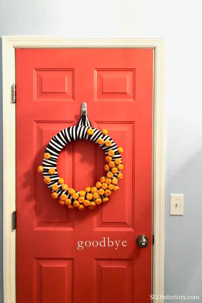 A colorful door wreath with black and white stripes and orange accents on a red door.