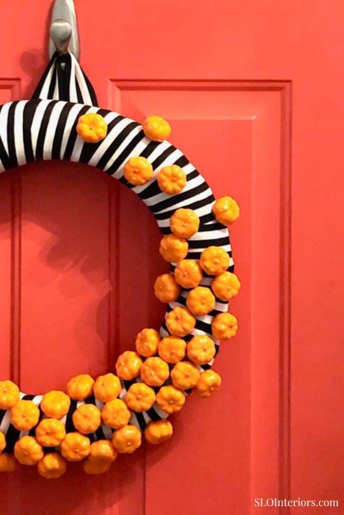 SLO Interiors decorative black and white striped wreath with orange accents on coral door.