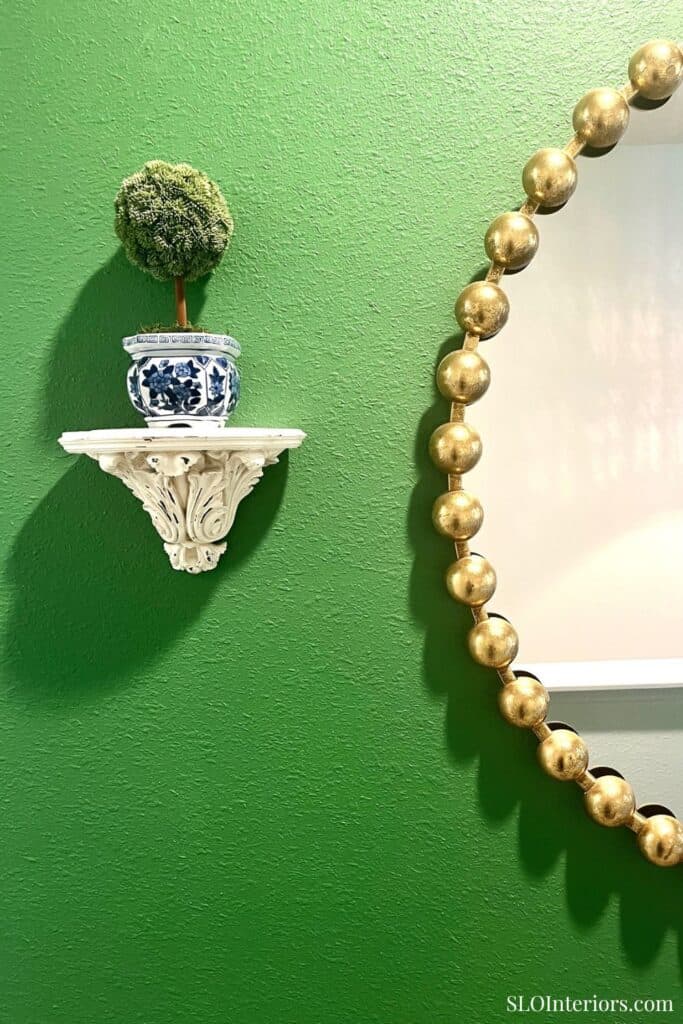 A lush green wall with decorative wall art including a small shelf with a potted moss ball and a gol.