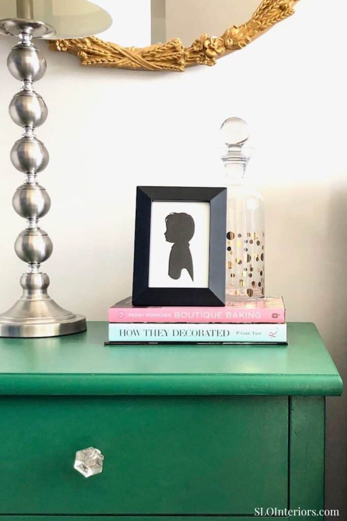 Elegant green side table with decorative items and framed silhouette artwork.