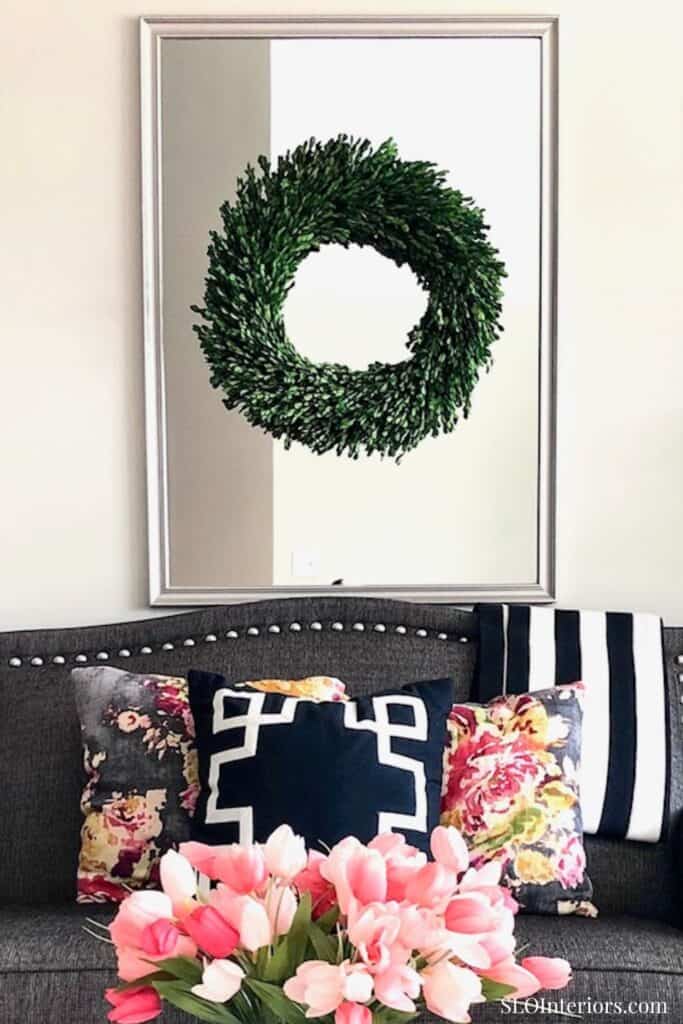 A lush green wreath hanging above a modern sofa with floral and geometric pillows, in a stylish livi.