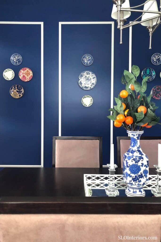 Elegant dining room with blue accent wall, decorative plates, and floral centerpiece.