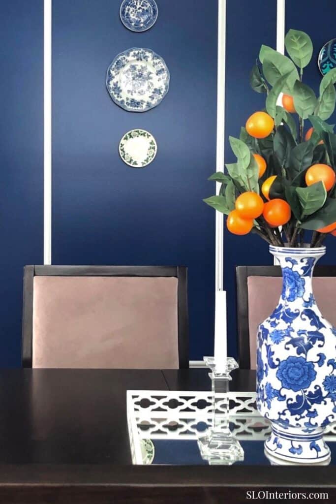 Elegant dining room with blue wall, decorative plates, and a floral vase with oranges.