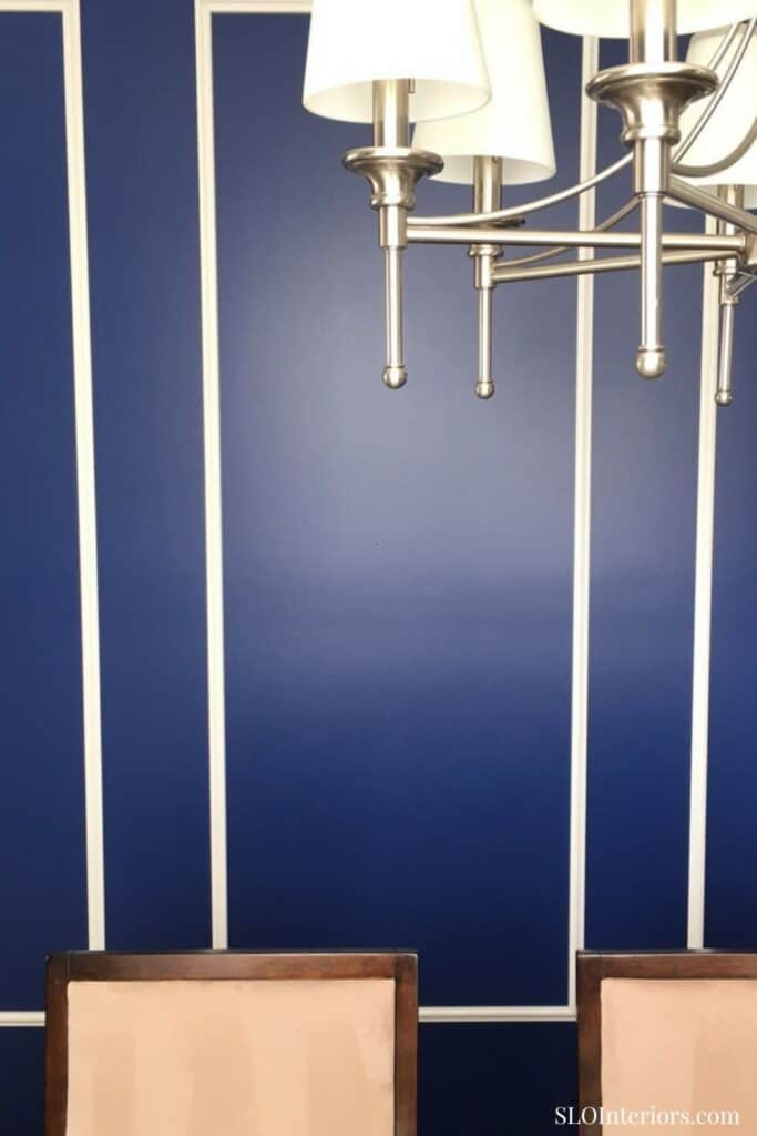 Modern chandelier with white lampshades over a navy blue wall with white vertical stripes.