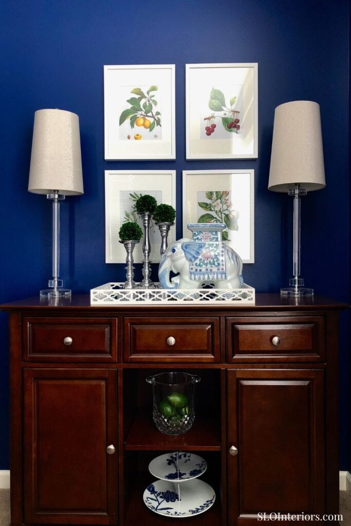 Elegant dark wood sideboard with decorative elephant figurine, framed botanical art, and table lamps.