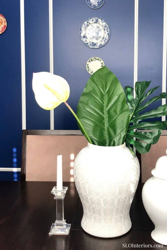 Elegant white ceramic vase with large green tropical leaves and a white calla lily, modern interior.