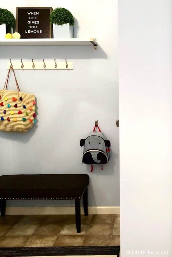 A colorful woven bag hanging on a wall hook in a modern entryway with a bench and decorative shelf.