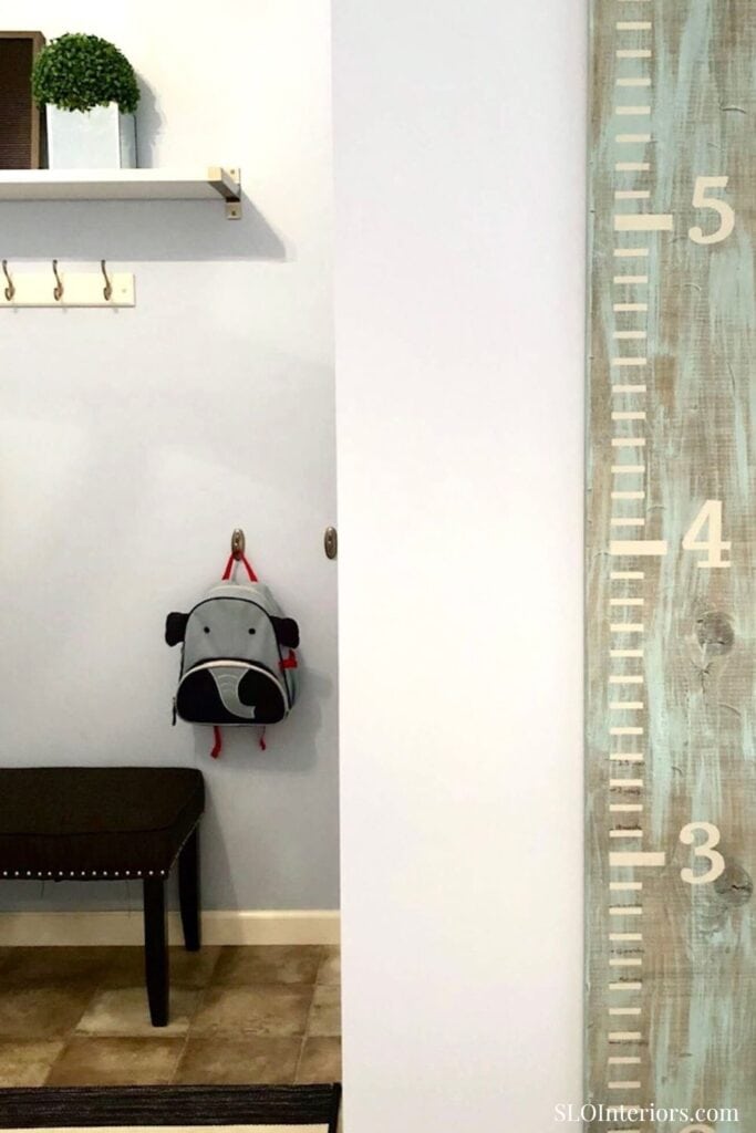 A modern interior corner with a height measurement wall, small bench, and wall-mounted backpack hold.