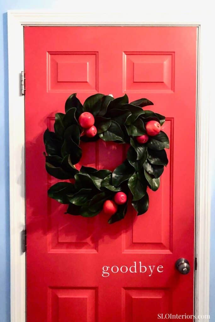 A lush green holiday wreath with red berries hanging on a vibrant red door.