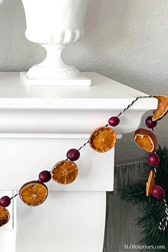 Festive holiday garland with dried orange slices and red berries on white mantel.