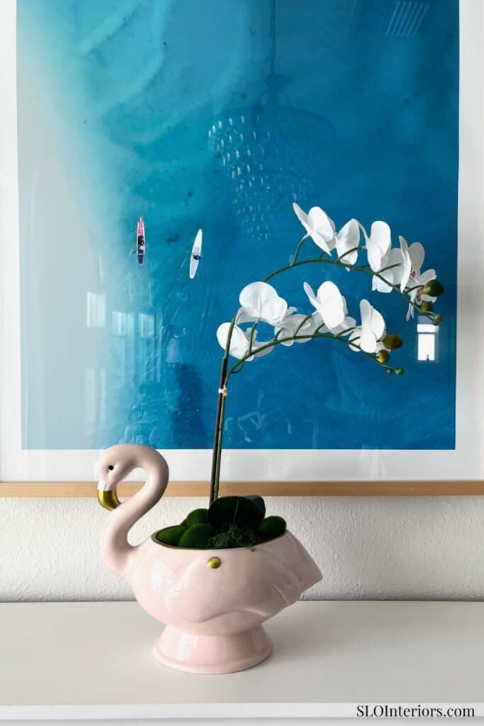Elegant white orchid in a pink swan-shaped ceramic vase with a blue abstract art background.