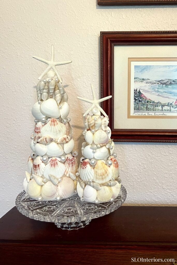 Seashell holiday centerpiece with starfish and coastal decor on glass cake stand.
