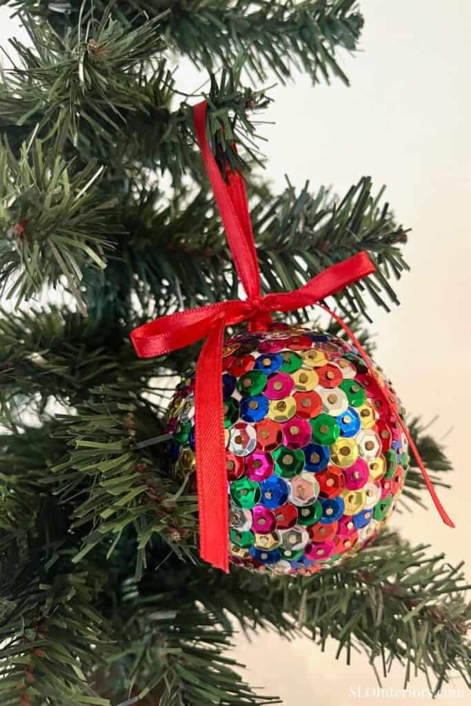 Festive sequin Christmas ornament with red ribbon on a Christmas tree.
