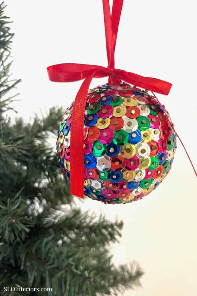 Brightly decorated Christmas ornament with sequins hanging on a Christmas tree branch.