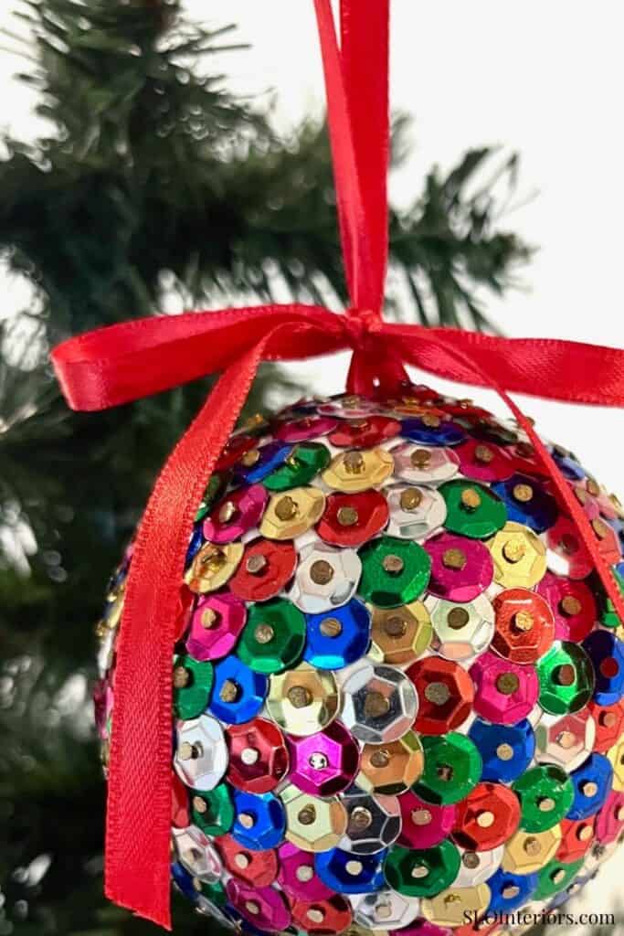 Festive sequin Christmas ornament hanging on a tree with a red ribbon bow.