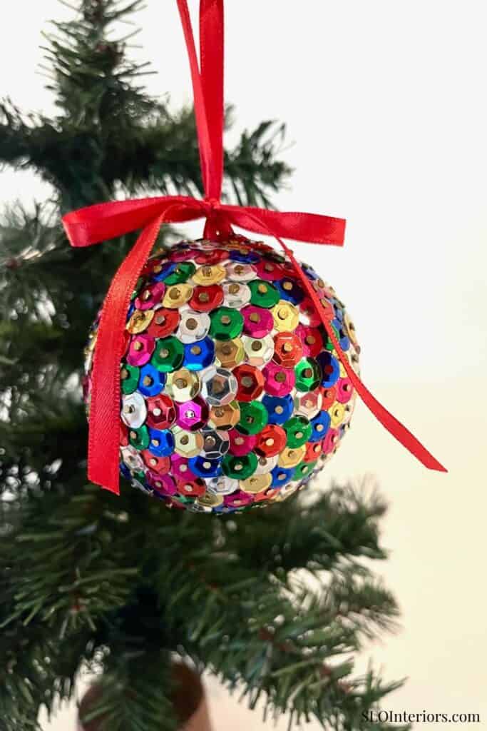 Festive Christmas ornament decorated with colorful sequins hanging on a Christmas tree.