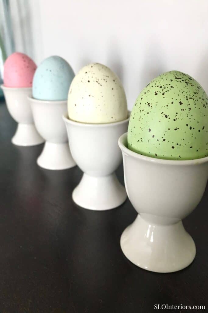 Pastel-colored speckled eggs in white egg cups, decorative home interior design.