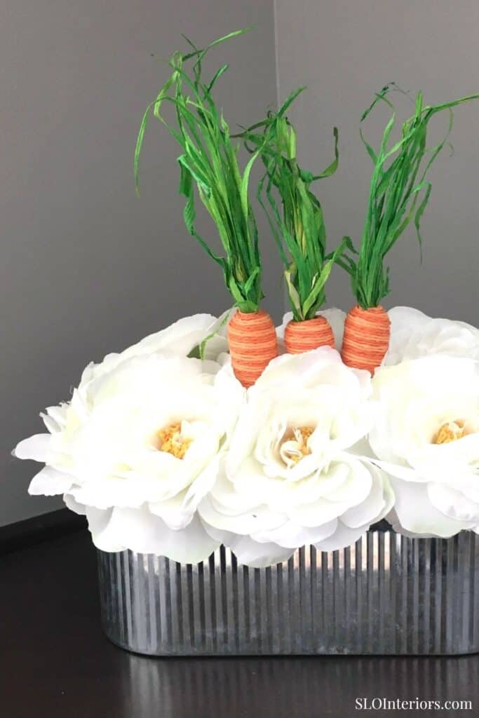 Fresh flower arrangement with carrots and greenery in a modern metallic vase.