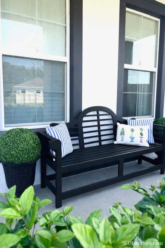 Black outdoor bench with striped and decorative pillows on a porch, modern home exterior.