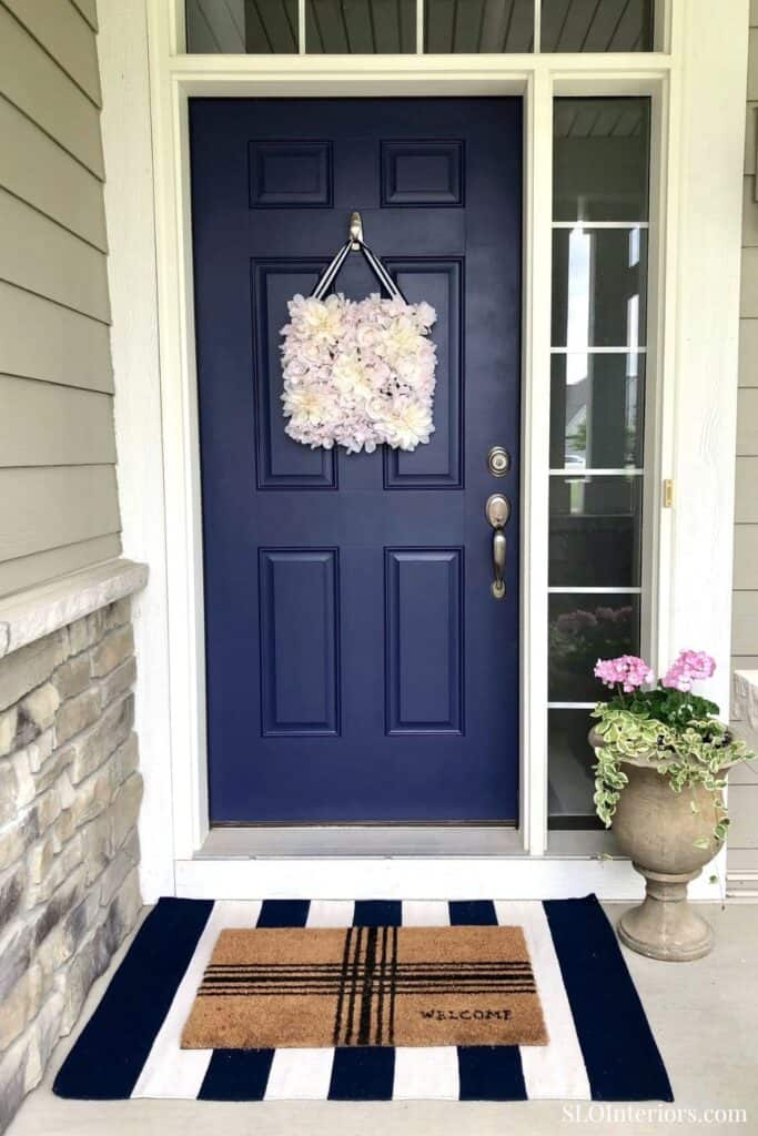 Bright blue front door with floral wreath and welcome mat, modern home entryway.
